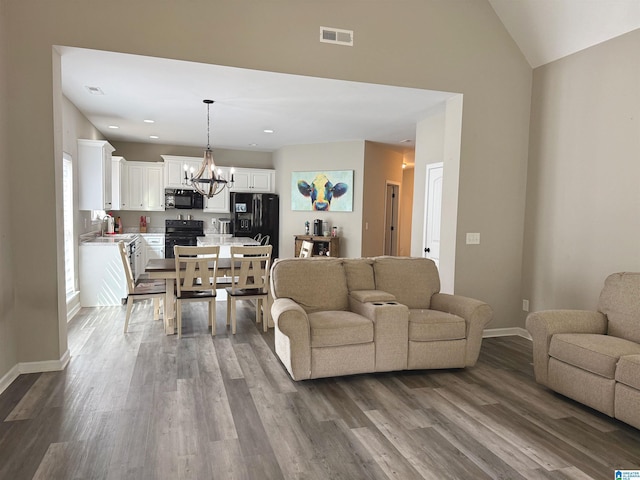 living room with hardwood / wood-style floors, vaulted ceiling, sink, and a chandelier