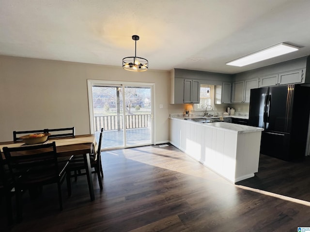 kitchen with pendant lighting, black refrigerator, gray cabinetry, dark hardwood / wood-style flooring, and kitchen peninsula