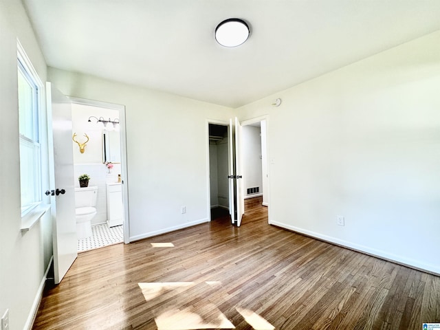 unfurnished bedroom featuring hardwood / wood-style flooring, connected bathroom, and a closet