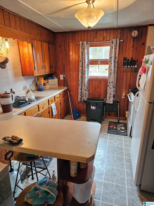 kitchen with white refrigerator, sink, kitchen peninsula, and wood walls