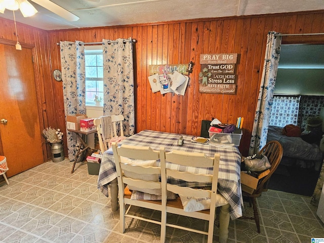 dining space with ceiling fan and wood walls