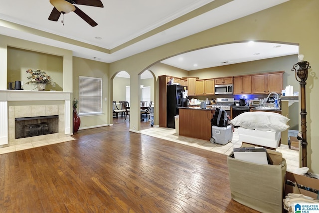 living room with crown molding, light hardwood / wood-style flooring, a raised ceiling, a tile fireplace, and ceiling fan