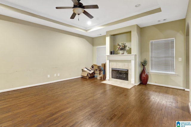 unfurnished living room featuring hardwood / wood-style floors, a tray ceiling, a fireplace, and ceiling fan