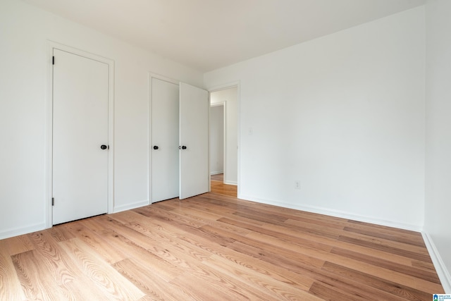 unfurnished bedroom with two closets and light hardwood / wood-style floors