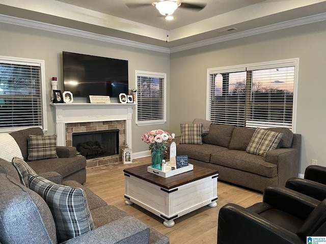 living room featuring a tile fireplace, wood-type flooring, ceiling fan, a raised ceiling, and crown molding