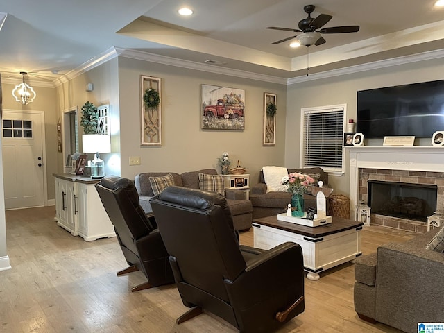 living room featuring a tiled fireplace, a tray ceiling, ornamental molding, and light wood-type flooring