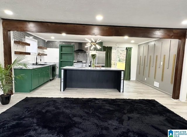 kitchen featuring wall chimney range hood, sink, appliances with stainless steel finishes, green cabinets, and beamed ceiling