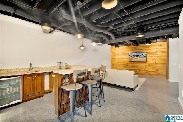 interior space with wine cooler, sink, light stone countertops, and wood walls