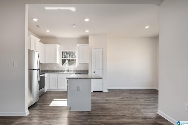 kitchen featuring appliances with stainless steel finishes, sink, white cabinets, dark stone counters, and a center island