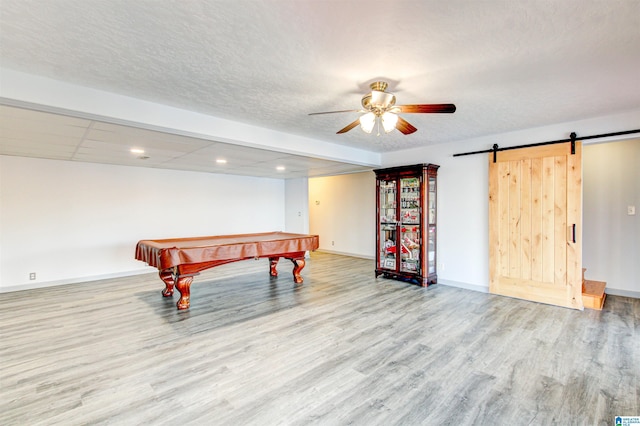 recreation room with billiards, a textured ceiling, ceiling fan, a barn door, and light hardwood / wood-style floors