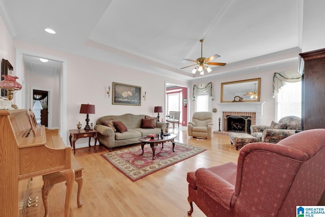 living room featuring ceiling fan, a fireplace, wood-type flooring, ornamental molding, and a raised ceiling