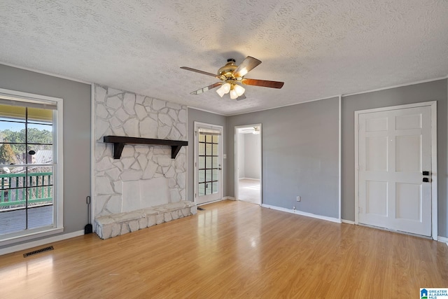 unfurnished living room with a stone fireplace, light hardwood / wood-style flooring, a textured ceiling, and ceiling fan