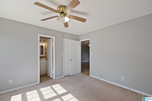 unfurnished bedroom with light carpet, ceiling fan, ensuite bath, and a textured ceiling