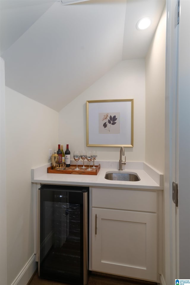 bar with sink, vaulted ceiling, beverage cooler, and white cabinets