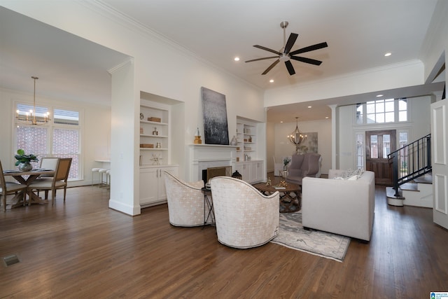 living room with crown molding, dark wood-type flooring, ceiling fan with notable chandelier, and built in features