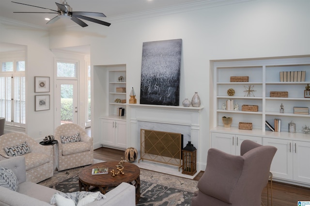 living room with a fireplace, ornamental molding, ceiling fan, dark wood-type flooring, and built in shelves