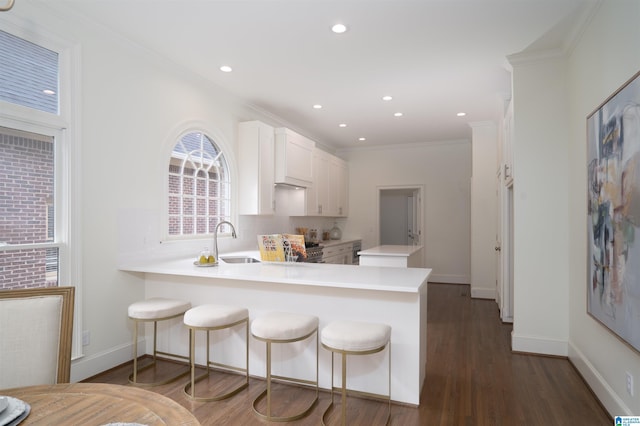 kitchen featuring a breakfast bar, white cabinetry, ornamental molding, dark hardwood / wood-style flooring, and kitchen peninsula