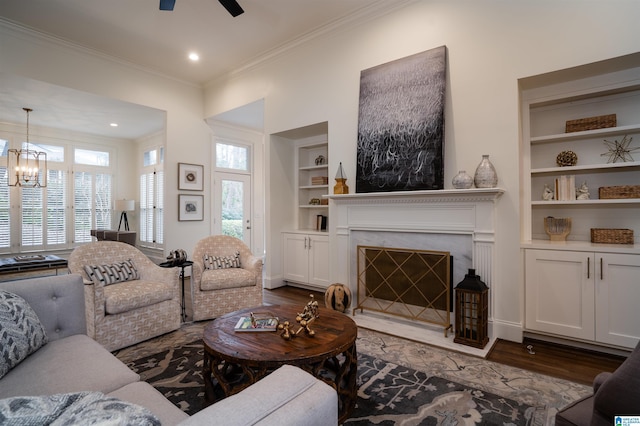 living room featuring ornamental molding, dark wood-type flooring, ceiling fan with notable chandelier, and built in features