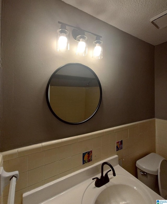 bathroom with tile walls, sink, toilet, and a textured ceiling