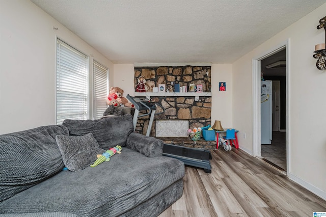 living room with a stone fireplace, a textured ceiling, and light wood-type flooring