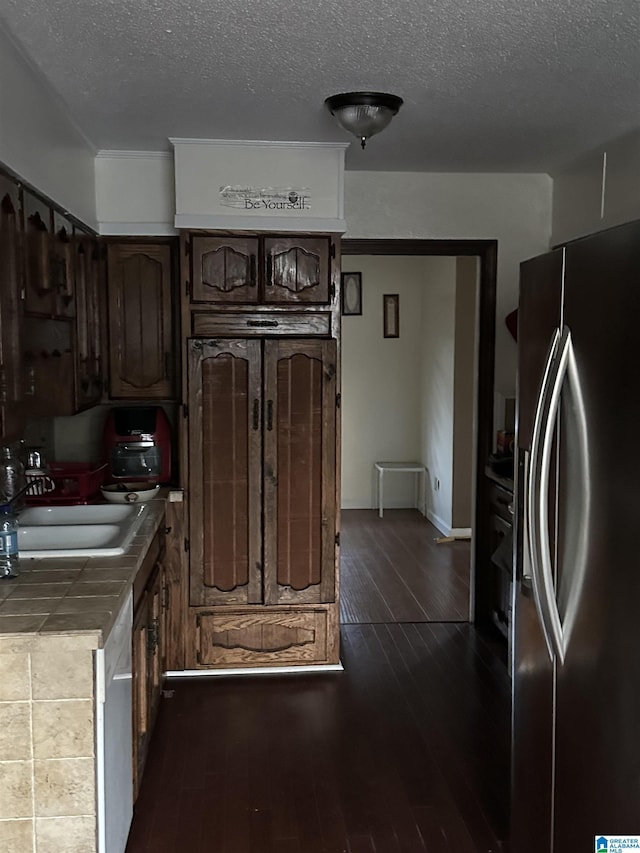 kitchen with sink, tile countertops, stainless steel fridge with ice dispenser, dark brown cabinets, and dark hardwood / wood-style floors