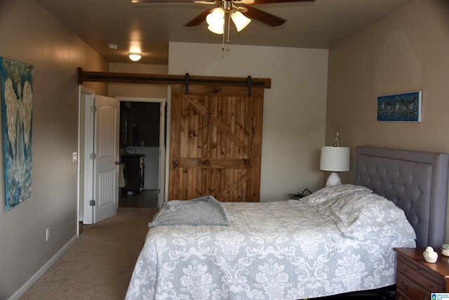 carpeted bedroom with a barn door, a ceiling fan, and baseboards