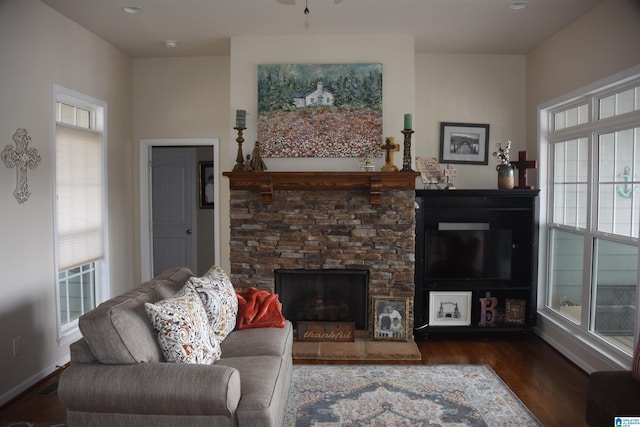 living room featuring a stone fireplace, dark wood-style flooring, and baseboards