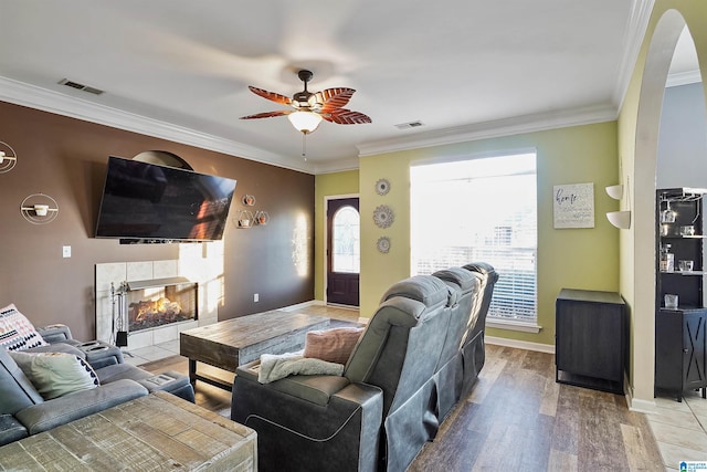 living room featuring ceiling fan, ornamental molding, a tiled fireplace, and wood-type flooring