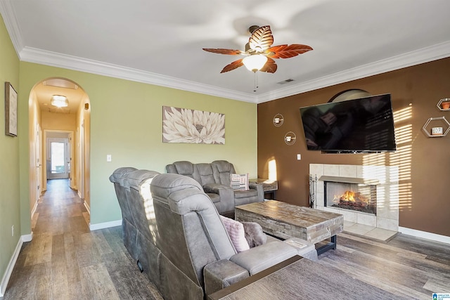 living room with hardwood / wood-style flooring, a tile fireplace, ornamental molding, and ceiling fan