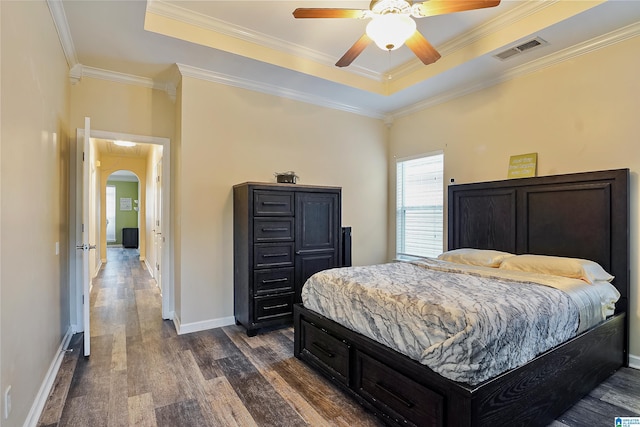 bedroom with ornamental molding, dark wood-type flooring, ceiling fan, and a tray ceiling