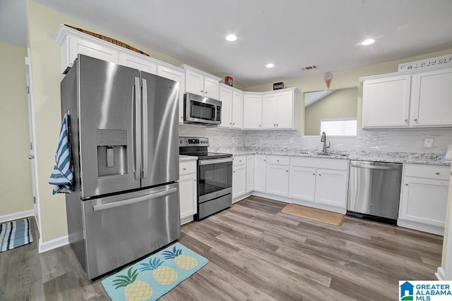 kitchen with appliances with stainless steel finishes, sink, white cabinets, decorative backsplash, and light stone counters