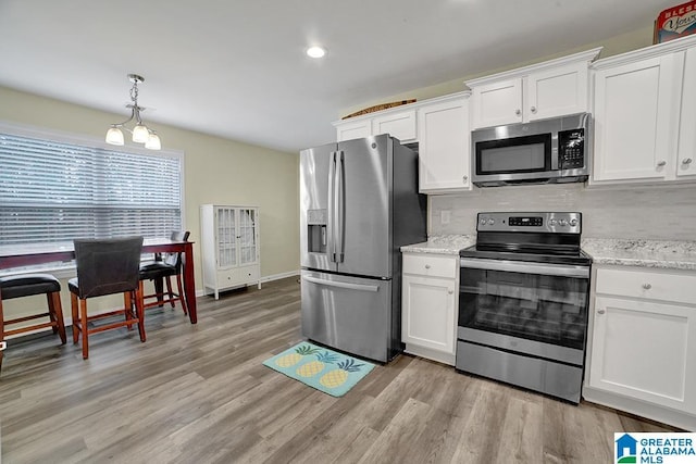 kitchen with white cabinetry, hanging light fixtures, light wood-type flooring, stainless steel appliances, and light stone countertops