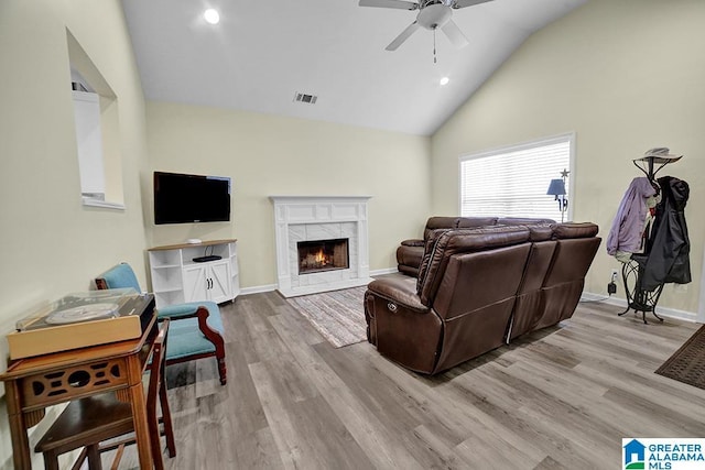 living room with light hardwood / wood-style flooring, high vaulted ceiling, a premium fireplace, and ceiling fan