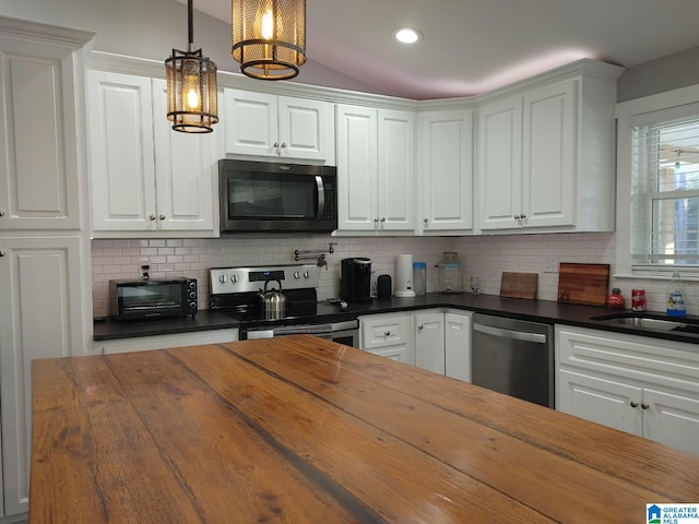 kitchen with appliances with stainless steel finishes, pendant lighting, tasteful backsplash, white cabinetry, and wooden counters