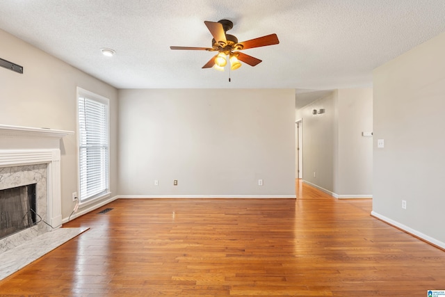 unfurnished living room featuring a textured ceiling, a high end fireplace, light hardwood / wood-style floors, and ceiling fan