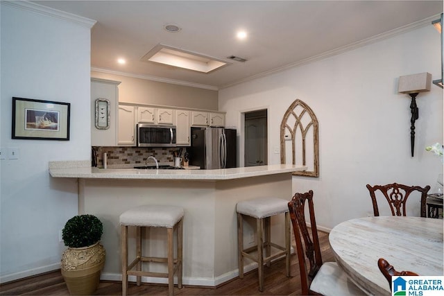 kitchen with appliances with stainless steel finishes, tasteful backsplash, white cabinets, a kitchen bar, and ornamental molding