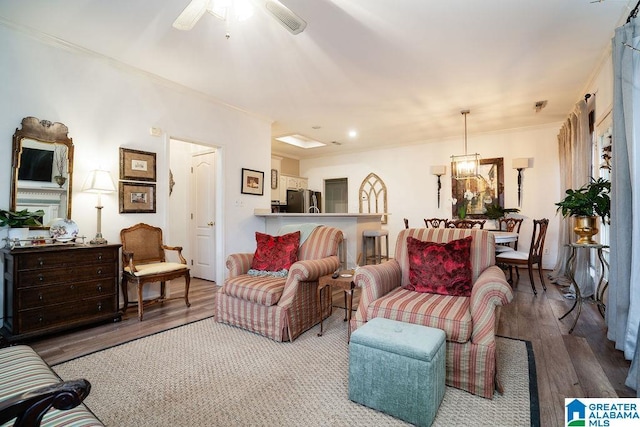 living room featuring crown molding, wood-type flooring, and ceiling fan with notable chandelier