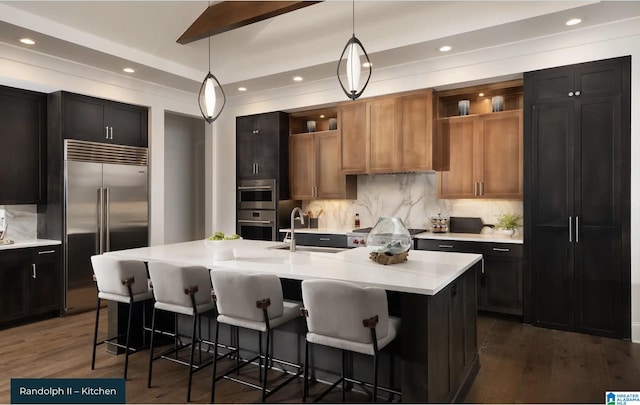 kitchen with sink, dark wood-type flooring, stainless steel appliances, an island with sink, and decorative light fixtures