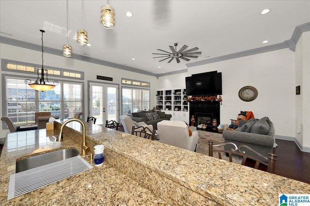 kitchen with decorative light fixtures, sink, ornamental molding, light stone countertops, and a healthy amount of sunlight