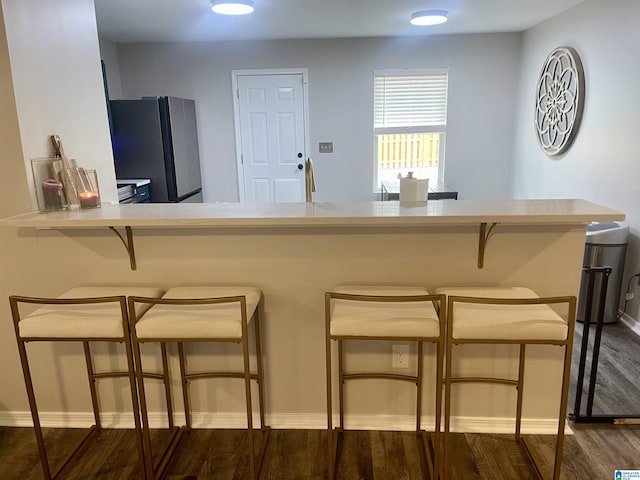 kitchen featuring baseboards, a kitchen breakfast bar, dark wood-style flooring, freestanding refrigerator, and light countertops