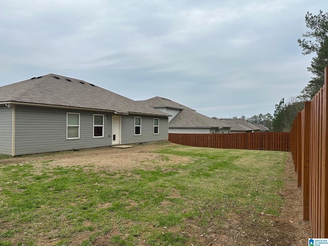 back of property with a yard, a shingled roof, and a fenced backyard