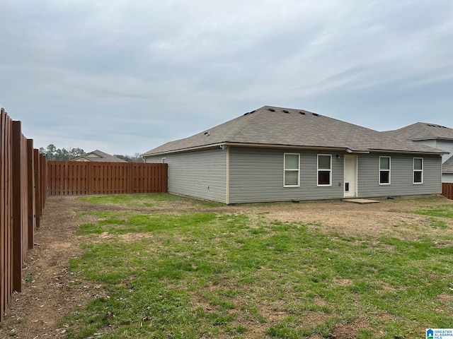 back of property with a shingled roof, a lawn, and a fenced backyard