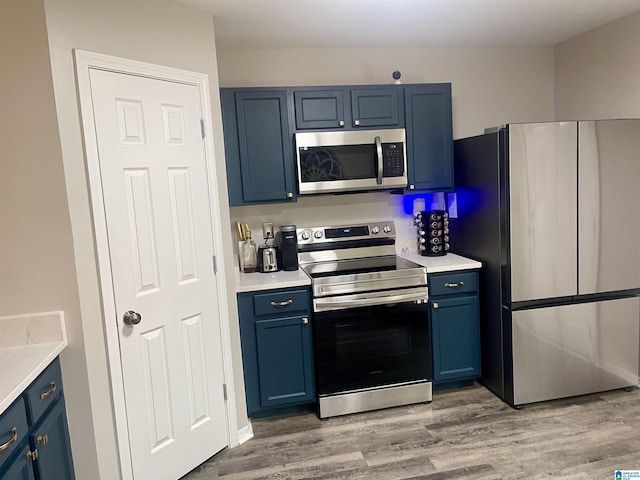 kitchen featuring stainless steel appliances, blue cabinets, light countertops, and wood finished floors