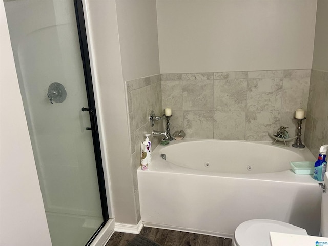 bathroom with toilet, a garden tub, a shower stall, and wood finished floors