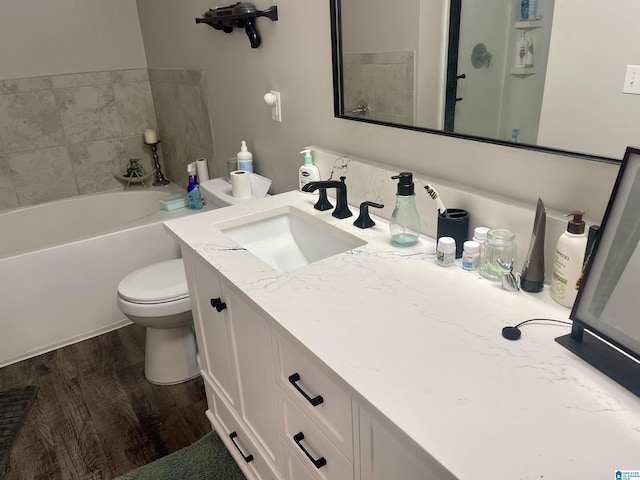 bathroom with toilet, a tub to relax in, wood finished floors, and vanity