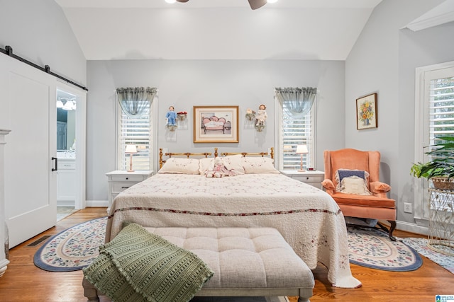 bedroom featuring multiple windows, a barn door, lofted ceiling, and light hardwood / wood-style flooring