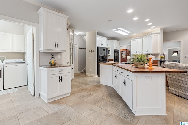 kitchen with wood counters, black refrigerator with ice dispenser, washer and dryer, and white cabinets