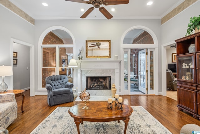 living room featuring a premium fireplace, crown molding, hardwood / wood-style flooring, and ceiling fan