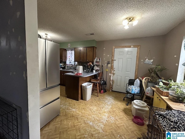 kitchen with a kitchen bar, a textured ceiling, stainless steel fridge, a kitchen island, and light parquet floors