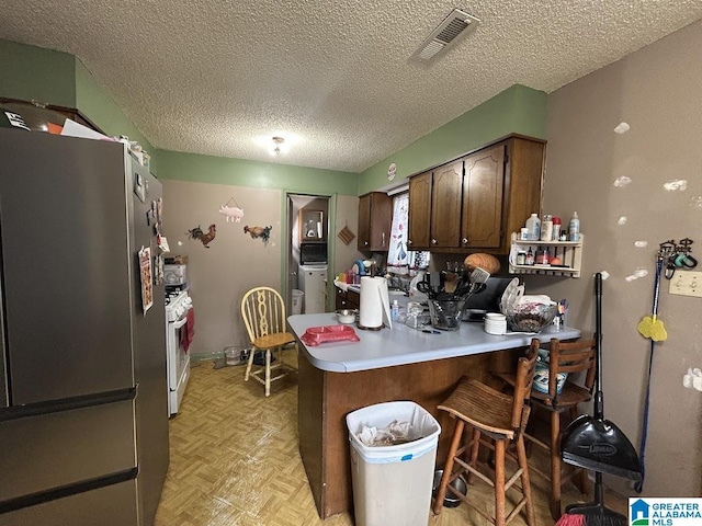 kitchen with stainless steel fridge, a kitchen bar, kitchen peninsula, light parquet flooring, and white gas stove